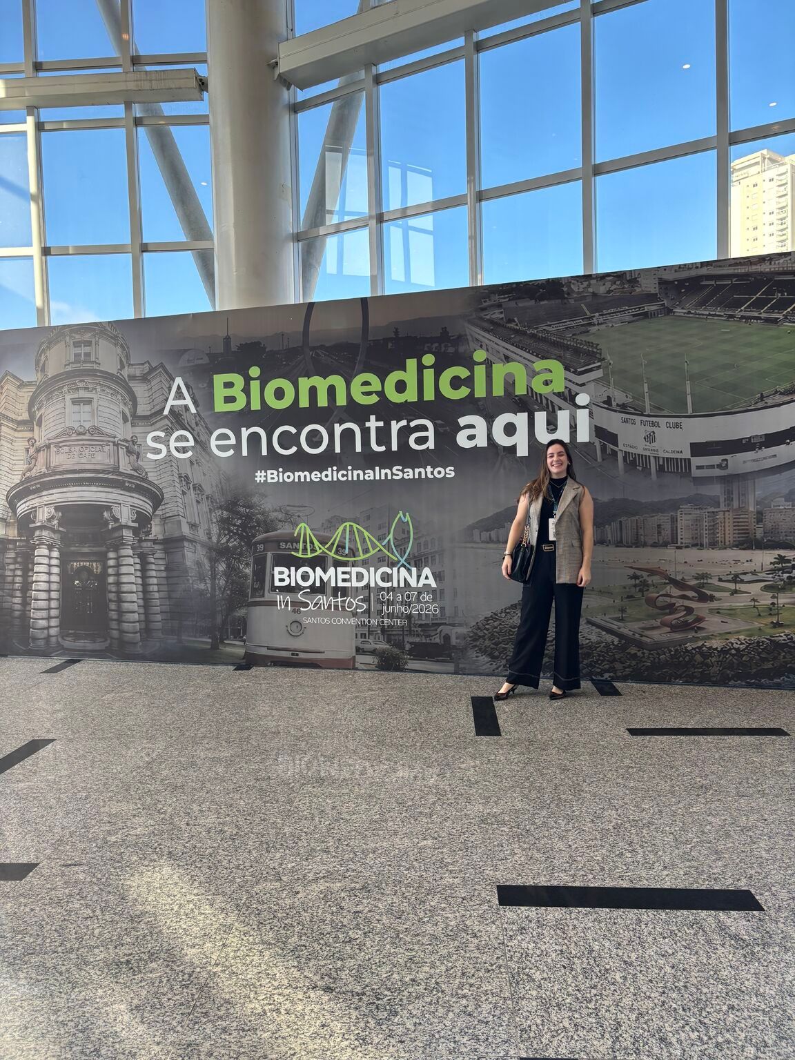 Isabela in front of the Biomedicina in Santos banner at the Santos Convention Center.